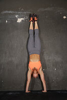 Junge Frau bei Fitnessübung Handstand an der Wand