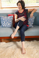 Brünette Frau in Spitzentop und Leggings sitzt auf grauer Couch