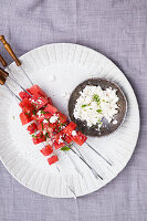 Grilled watermelon with mint on sticks at a big white ceramic plate and feta in a little bowl