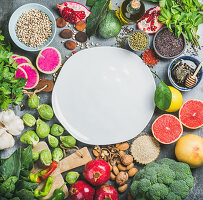 Stillleben mit Gemüse, Obst, Samen, Getreide, Gewürzen, Superfoods und Kräutern um einen weissen Teller