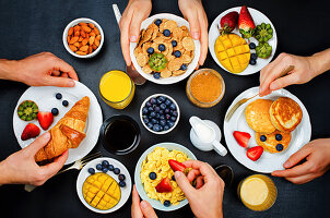 Breakfast table setting with flakes, juice, croissants, pancakes and fresh berries
