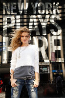 A young blonde woman wearing a t-shirt, a white jumper and jeans