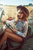 A brunette woman wearing a hat, a sparkly blouse and short sitting in a jeep