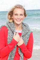 A young blonde woman wearing a red jumper with a grey jumper over her shoulders