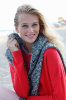 A young blonde woman wearing a red jumper with a grey jumper over her shoulders