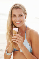 A mature blonde woman on a beach wearing a bikini and holding an ice cream