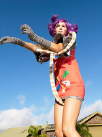 Junge Frau mit lila Haaren in buntem, futuristischem Kleid und Handschuhen