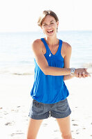 A mature brunette woman on a beach wearing a blue top and a silver bracelet