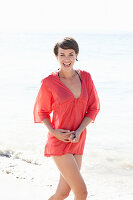 A mature brunette woman on a beach wearing a red shirt and a black bathing suit