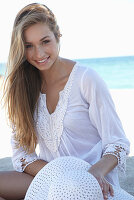 A young blonde woman on a beach wearing a white summer dress and a white summer hat