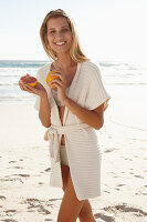 Reife blonde Frau mit Grapefruit in Dessous und Strickjacke am Strand