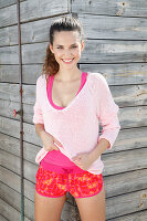 A brunette woman wearing a pink jumper, a top and shorts