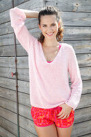 A brunette woman wearing a pink jumper and shorts