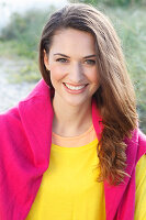 A brunette woman wearing a yellow jumper with a pink jumper over her shoulders