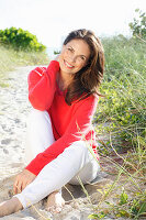 Brunette woman wearing red knit sweater and white trousers