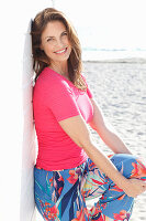 Brunette woman wearing pink T-shirt and multicoloured trousers on beach