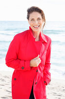 Brünette Frau in rotem Trenchcoat am Strand
