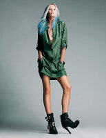 A young woman with dip-dyed hair wearing a short, green playsuit and high-heeled boots