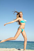 Junge blonde Frau im türkisen Bikini und weißem Sommerhut am Strand