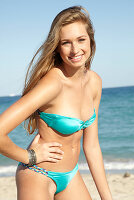 A young blonde woman on a beach wearing a turquoise bikini