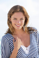 A young brunette woman on a beach wearing a black-and-white striped top