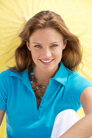 A young brunette woman wearing a blue shirt in front of a yellow parasol