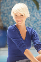 A mature blonde woman with short hair wearing a blue top against a blue background