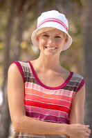 Reife, kurzhaarige blonde Frau im gestreiften Shirt und Hut im Grünen