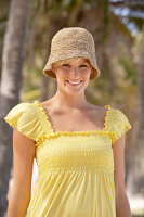 A mature blonde woman with short hair outside wearing a yellow top and a hat