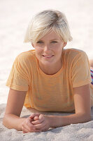 Reife, kurzhaarige blonde Frau im gestreiften Bikini und orangenem Shirt am Strand