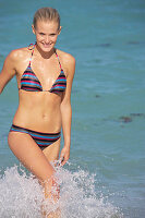 A mature blonde woman with short hair on a beach wearing a striped bikini