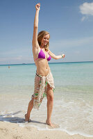 Junge blonde Frau im lila Bikini und Strandtuch um die Hüften am Strand