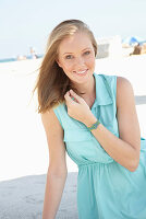 A young blonde woman on a beach wearing a light-blue summer dress