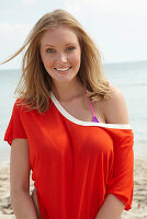 A young blonde woman on a beach wearing a purple bikini and an orange top