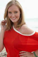 Junge blonde Frau im lila Bikini und orangenem Top am Strand
