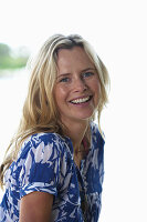 A young blonde woman on a beach wearing a blue-and-white patterned shirt