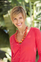 A mature woman with short blonde hair outside wearing a red shirt