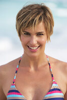 A mature woman with short blonde hair on a beach wearing a bikini