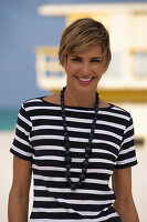 Junge Frau mit kurzen blonden Haaren im schwarz-weiß gestreiften Top am Strand