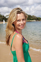 Junge blonde Frau im grünen Top und rosa Bikini am Strand