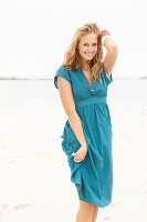 A young blonde woman on a beach wearing a blue summer dress