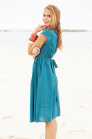 Junge blonde Frau im blauen Sommerkleid am Strand