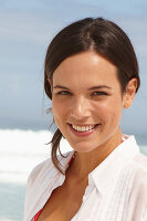 A young brunette woman on a beach wearing a white summer dress