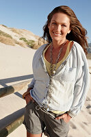 A brunette woman on a sandy beach wearing a light blouse and shorts