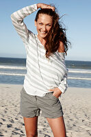 A brunette woman on a sandy beach wearing a striped top and shorts