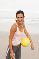 Junge brünette Frau mit Ball in sportlicher Kleidung am Meer