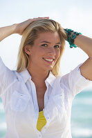 A young blonde woman on a beach wearing a white blouse