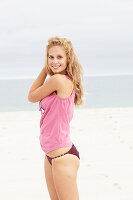 Junge blonde Frau im rosa Top und Bikini am Strand