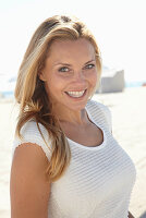 A mature blonde woman on a beach wearing a white top