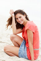 A brunette woman on a beach wearing a salmon-coloured top and a denim skirt